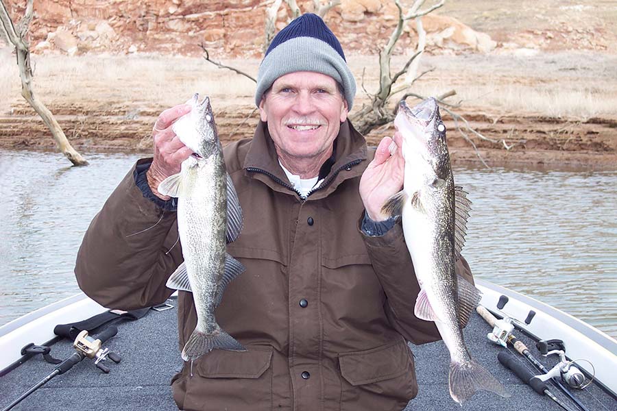 Wayne Gustaveson holding two freshly caught walleye in a boat at Lake Powell