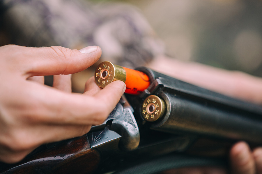 A hunter loading two 16-gauge shotgun shells into a shotgun