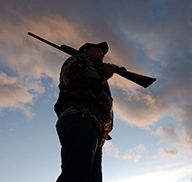 Silhouette of a hunter in a field, carrying a rifle