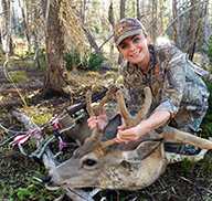 Woman with archery equipment and harvested buck deer