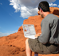 Man sitting near Utah's red rocks, browsing the Utah Hunt Planner on his laptop
