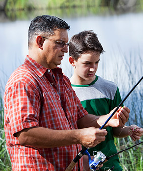 Father and son standing at a pond, holding fishing poles