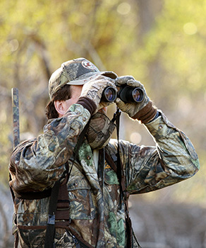 Hunter in a forest wearing camouflage, holding binoculars