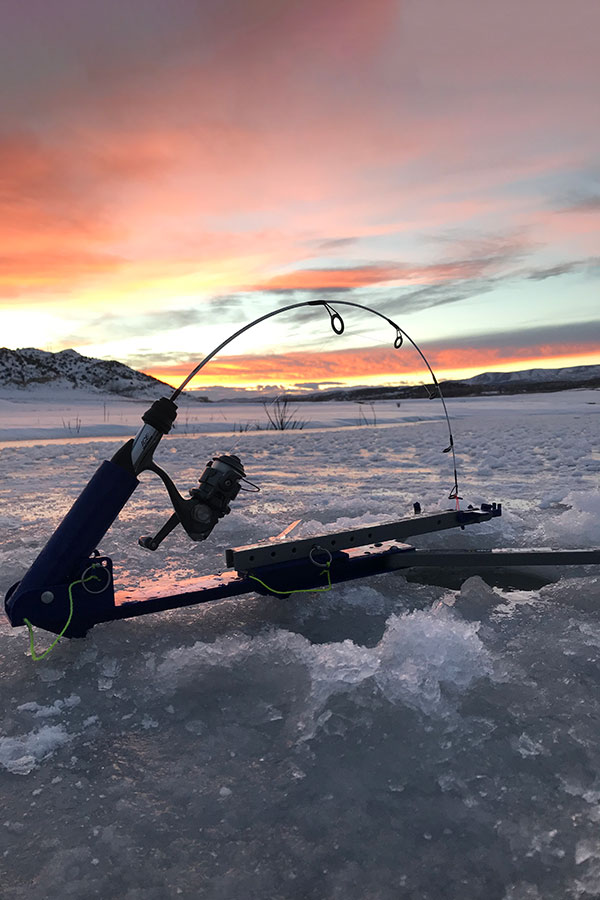 Fishing pole set up in a hole in a drilled hole in the ice, at sunset
