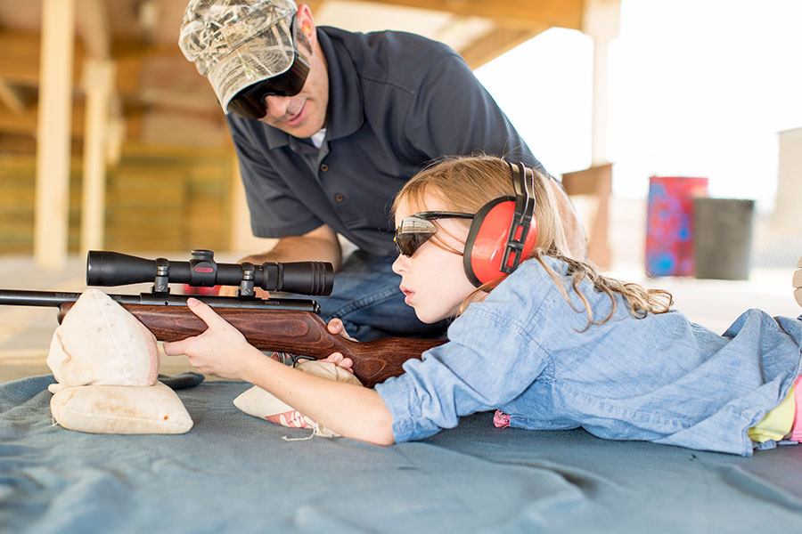 Girl at Lee Kay Public Shooting Range, aiming a rifle with a scope while being guided by a mentor
