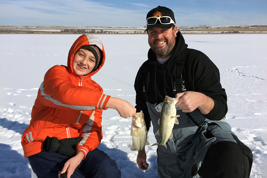 Father and son holding largemouth bass while ice fishing over a frozen lake