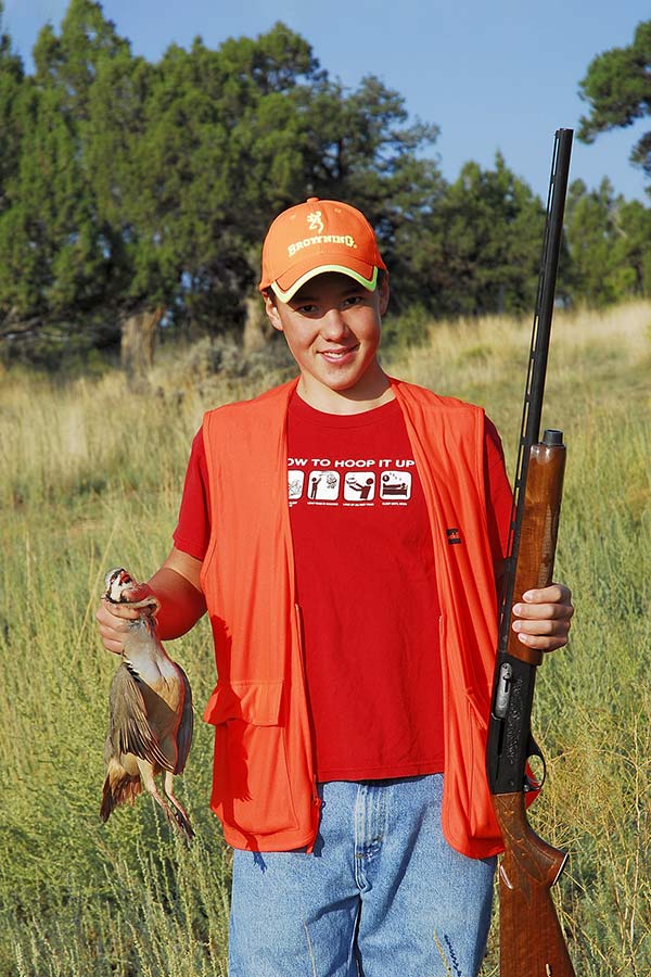 Youth upland game hunter holding a harvested bird and a shotgun
