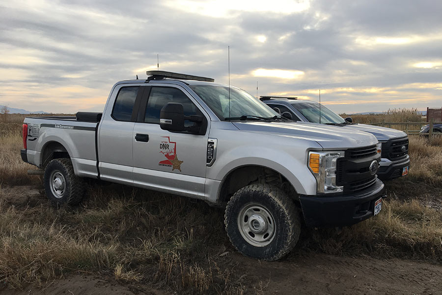 Two Utah of Division Wildlife Resources law enforcement trucks parked in a field under a cloudy sky